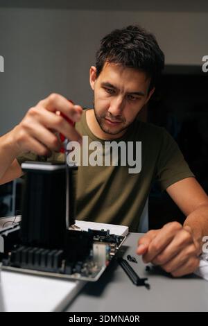 Vertical shot of serious computer technician carefully installing CPU cooler onto motherboard, performing essential maintenance and upgrades on Stock Photo