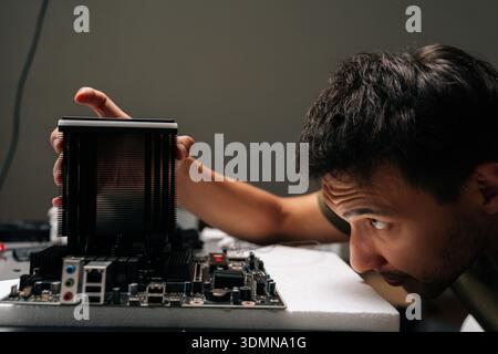 Close-up of computer technician male installing CPU cooler onto motherboard, performing maintenance and repair work on desktop computer in dark Stock Photo