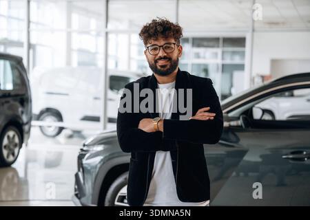 Confident car salesman using digital tablet inside modern showroom. Stock Photo