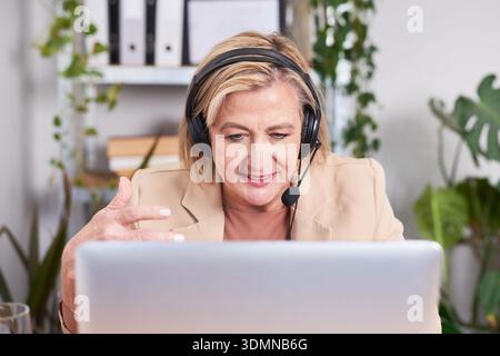 Businesswoman With Headset Working On Laptop In Modern Office, Engaged In Video Call Stock Photo