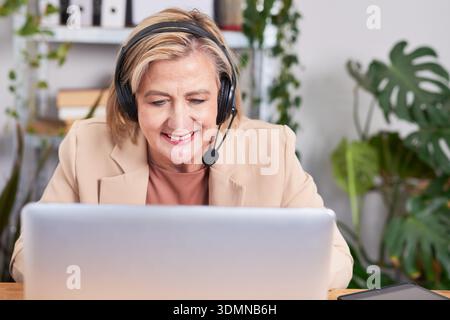 Professional Woman With Headset Working at Laptop in Modern Office, Customer Support, Remote Assistance Stock Photo
