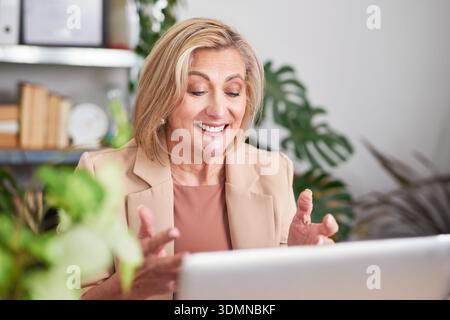 Confident Senior Woman In Beige Blazer Working On Laptop In Modern Office Stock Photo