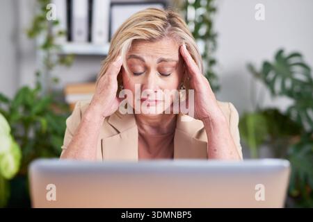 Professional Woman Stressed at Laptop in Office, Head in Hands, Burnout Concept Facing Work Challenges Today Stock Photo
