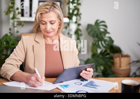 Businesswoman Working at Desk with Tablet, Analyzing Documents in Office Stock Photo