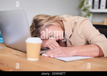 Tired Office Worker Resting On Desk With Laptop, Coffee Cup, And Paperwork At Work Today Stock Photo