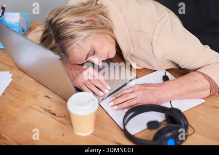 Fatigued Professional Resting on Laptop At Desk With Notebook And Coffee Cup Stock Photo