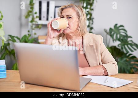 Business Woman Taking Coffee Break While Working On Laptop At Modern Office Desk Stock Photo