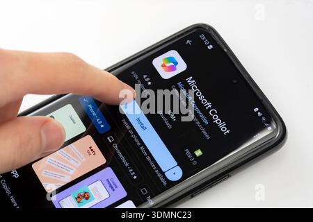 Microsoft Copilot AI assistant app page on Google Play Store, hand pressing install button closeup. Downloading artificial intelligence software on a Stock Photo