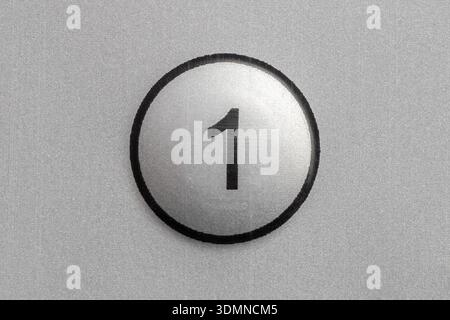 Round silver push button with number 1 on a metallic panel, simple control key on electronic device, closeup symbol on textured background, minimal us Stock Photo