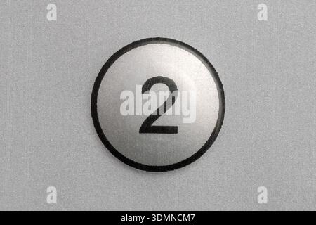 Round silver push button with number 2 on metallic panel, simple control key on generic electronic device, remote channel selection symbol macro close Stock Photo