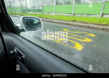 View from inside a car through rain-speckled side window onto wet city street with large yellow BUS lane road marking, curb and green sound barrier fe Stock Photo