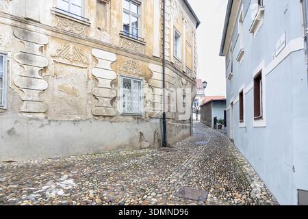 A narrow cobblestone alley between pale walls, featuring vintage street lamps and simple windows. This quaint, historic passage evokes urban nostalgia Stock Photo