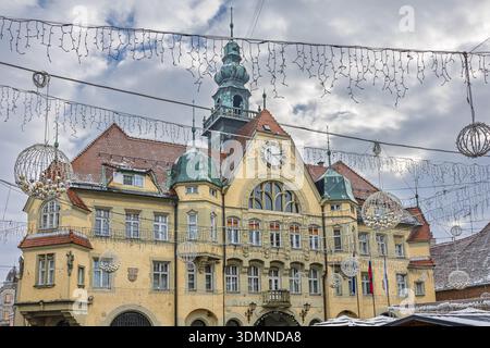 A grand yellow town hall adorned with festive lights and hanging ornaments, creating a cheerful winter scene. Clock tower, green domes, and arched win Stock Photo