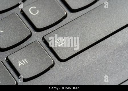 Laptop keyboard backlight toggle key closeup with illumination icon on spacebar, black matte plastic keys, computer shortcut hotkey button, technology Stock Photo