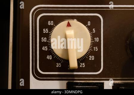 Old vintage mechanical 60 minute timer dial with cream turn knob and red pointer on black appliance control panel, closeup front view of analog countd Stock Photo