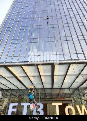 Workers cleaning the exterior glass panels of the FTB tower in Phnom Penh, Cambodia. The location is a prominent commercial area in the city. Stock Photo
