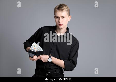 Young businessman in shirt with wallet full of dollar banknotes on grey background Stock Photo