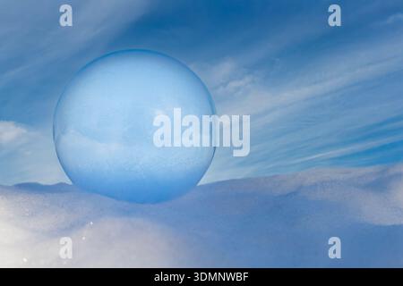 Frozen Soap Bubble Resting on Snow with Beautiful Blue Sky Stock Photo