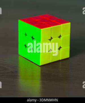 A colorful Rubik's Cube with red, green, and yellow sides rests on a rustic wooden table, showcasing the iconic puzzle in natural light. Stock Photo