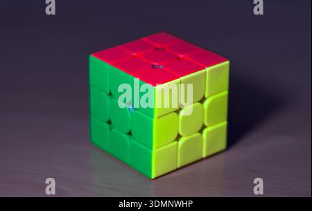 A colorful Rubik's Cube with red, green, and yellow sides rests on a rustic wooden table, showcasing the iconic puzzle in natural light. Stock Photo