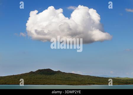 A large white cumulus cloud floating above Rangitoto Island across calm water in the Hauraki Gulf, Auckland, New Zealand. Stock Photo