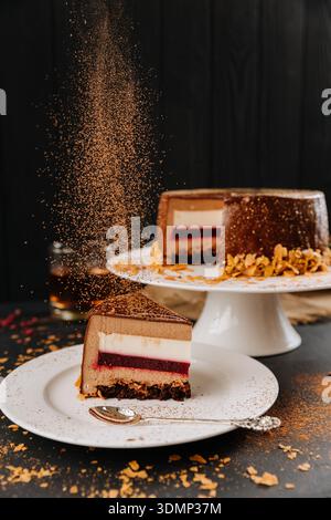 Layered chocolate mousse cake slice with berry layer and falling cocoa dust Stock Photo