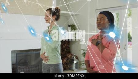 Practicing two women breathing in living room near hearth in fitness clothes, with digital overlay Stock Photo