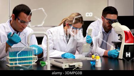 Pipetting lab team in lab coats, goggles, blue nitrile gloves handling plate and microscope in lab Stock Photo
