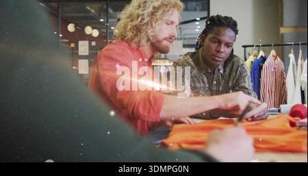 Reaching rust shirt designer trimming bright orange garment on table in design studio, with rack Stock Photo