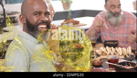 Smiling bearded man wearing light shirt sitting at kitchen table, with wooden platter and sparkles Stock Photo