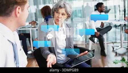 Gesturing senior woman wearing grey blazer holding tablet during meeting in office, speech graphics Stock Photo
