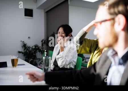Business meeting featuring diverse professionals in an office setting discussing ideas with drinks during the afternoon. Woman yawns. Stock Photo