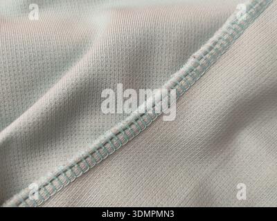 This is a close-up of a mint green shirt fabric with a teal overlock stitch seam. Stock Photo