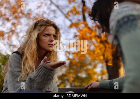 Two women engage in a serious conversation amidst vibrant autumn foliage, capturing a moment of connection and reflection during the golden hour Stock Photo