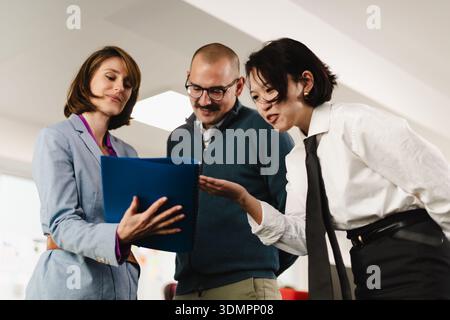 Three businesspeople collaborate on a project in a modern office setting, discussing plans and strategies during a productive meeting Stock Photo