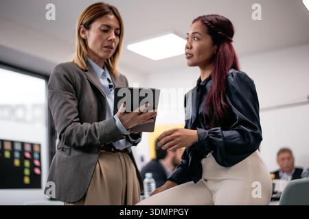 Two professionals collaborating in a modern office using a tablet device, showing a teamwork-focused discussion during workplace activities. Stock Photo