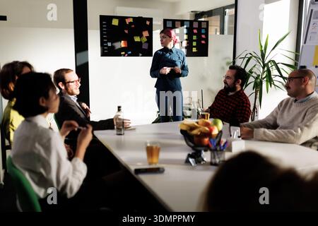 Business meeting in a modern office featuring a woman presenting ideas to a team of professionals during a brainstorming session in bright natural Stock Photo
