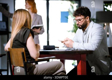 Business meeting in a modern office with two professionals discussing ideas and a third colleague engaged in the background Stock Photo