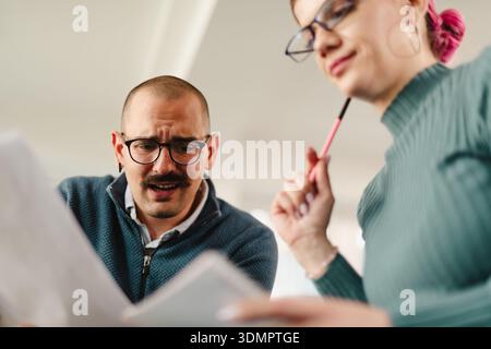 Collaboration between two business professionals in a modern office setting while discussing project details and analyzing reports Stock Photo