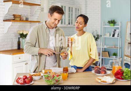 Couple preparing toast with jam and drinking juice together in bright kitchen Stock Photo