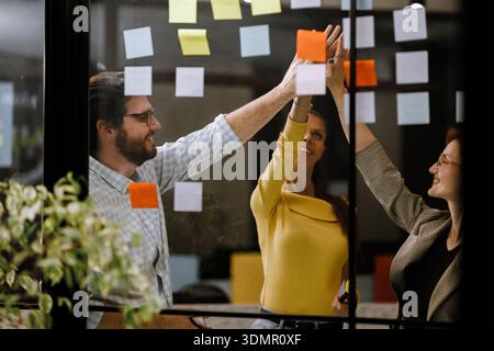 Team members collaborating on brainstorming session using sticky notes in modern office space during afternoon hours Stock Photo