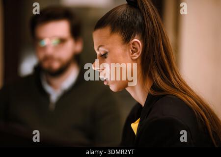 Focused young woman engaged in a discussion with a man in a dimly lit setting, highlighting attention and participation in a collaborative environment Stock Photo