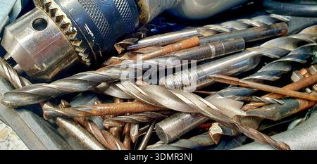 Pile of used drill bits and a drilling machine. Stock Photo