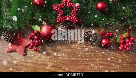 Displaying evergreen garland on wooden tabletop, showing red baubles, pine cones, metal star cutter Stock Photo