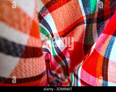 A macro shot of a folded plaid fabric with a pattern of red, white, and green stripes. The soft focus and textile weave highlight the material's textu Stock Photo