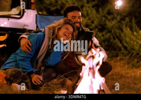 Couple enjoys a cozy evening by the campfire under the stars in a serene outdoor setting on a cool night Stock Photo