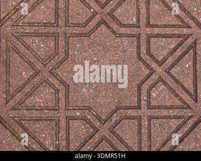 A top-down shot of a red concrete paving stone featuring an embossed eight-pointed star (octagram) design. The geometric pattern and gritty texture ar Stock Photo