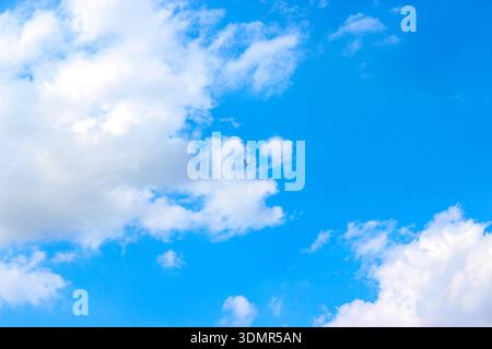 Background with clouds on blue sky. Sky view. Beautiful sunny sky. Clouds on blue sky. Sun shining through the puffy clouds. Airplane in the clouds. Stock Photo