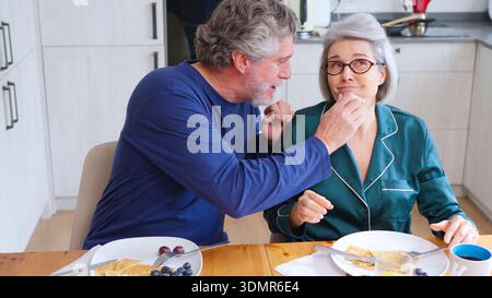 Loving senior couple sharing breakfast in kitchen at home Stock Photo