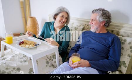 Senior couple sharing a joyful breakfast in bed Stock Photo